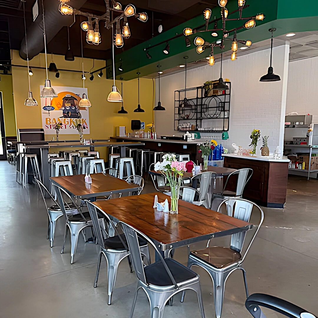A modern Birmingham restaurant interior with wooden tables, metal chairs, hanging lights, and a counter. Flowers decorate the tables, and a colorful wall mural enhances the space.