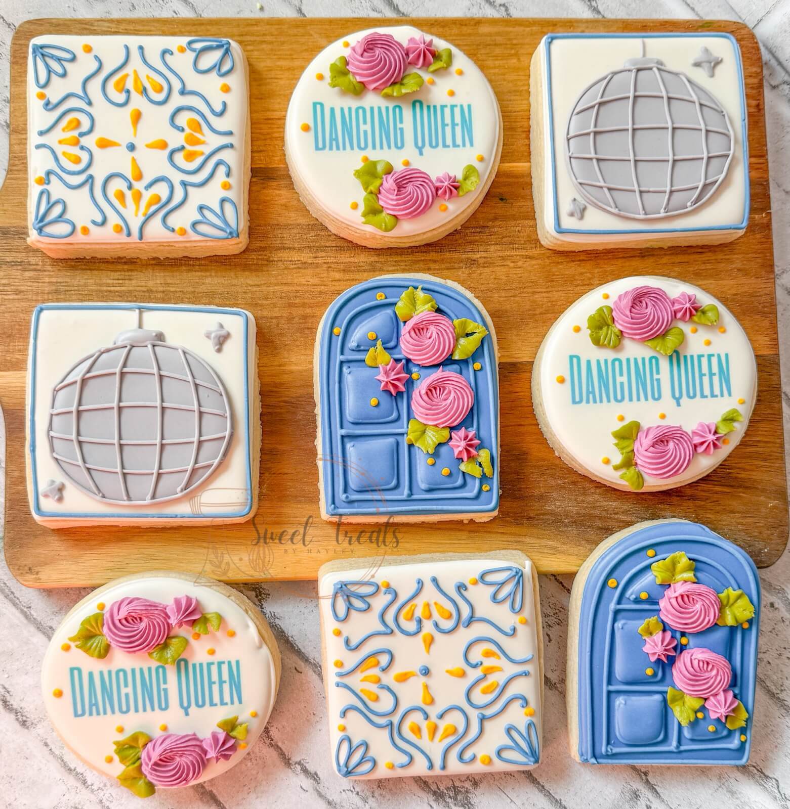 Decorated cookies featuring "Dancing Queen" text, disco balls, ornate blue doors with flowers, and intricate yellow and blue patterns on a wooden board—perfect treats inspired by the vibrant flair found in Birmingham restaurants.