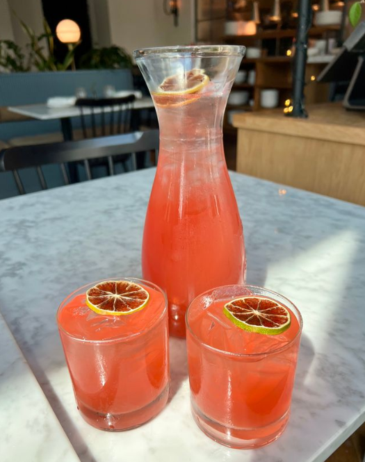 An orange juice carafe and two glasses with pink liquid and blood orange slice on top.
