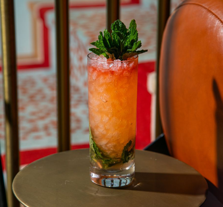 An orange and red liquid with crushed ice in tall glass garnished with mint leaves