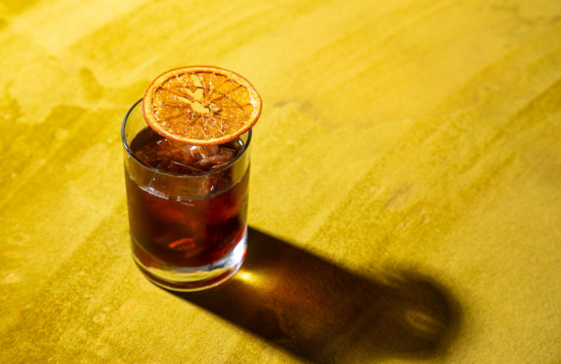 Brown liquid in short glass with ice cubes and dried orange slice as garnish.