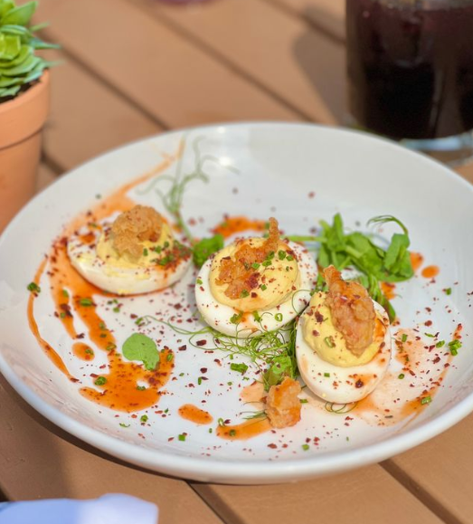 A plate of 3 crawfish deviled eggs garnished with red sauce and celery