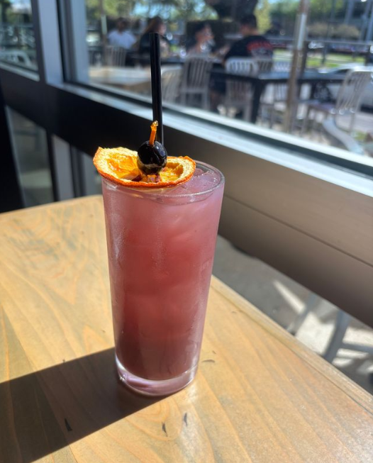 A glass with pink liquid and ice, garnished with an orange wheel slice