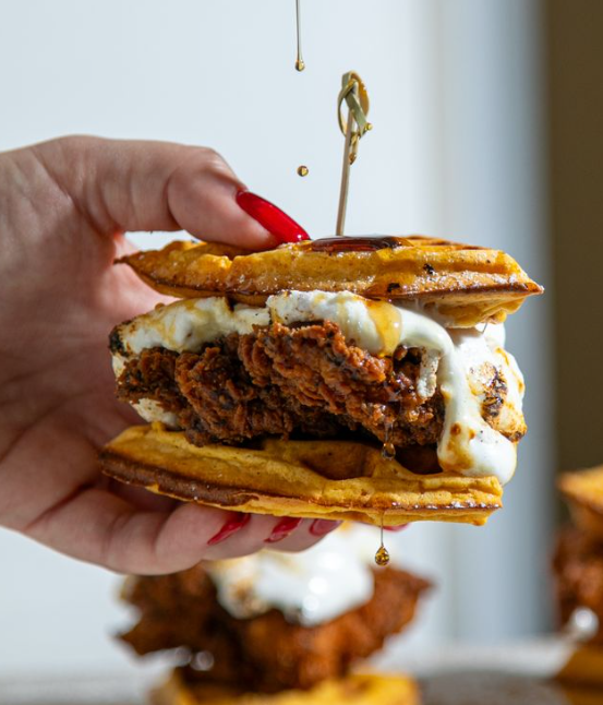 A woman's hand holding up a chicken and waffle slider, waffle being used for the bun with chicken in the middle and syrup running down.