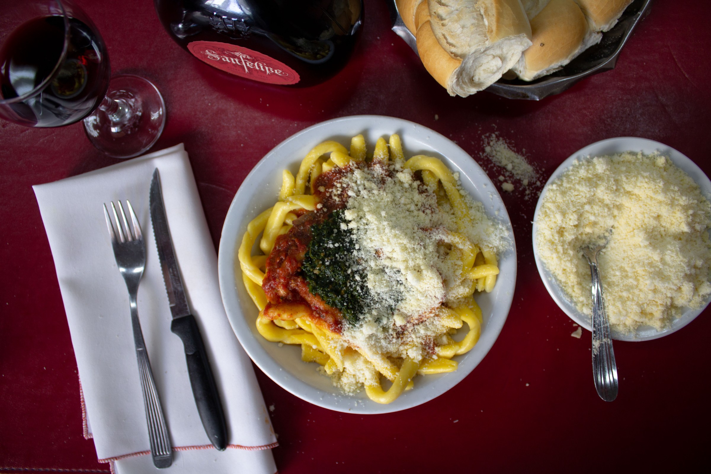 From above, a plate of pasta covered with grated cheese and sauces, beside a bowl of more grated cheese.