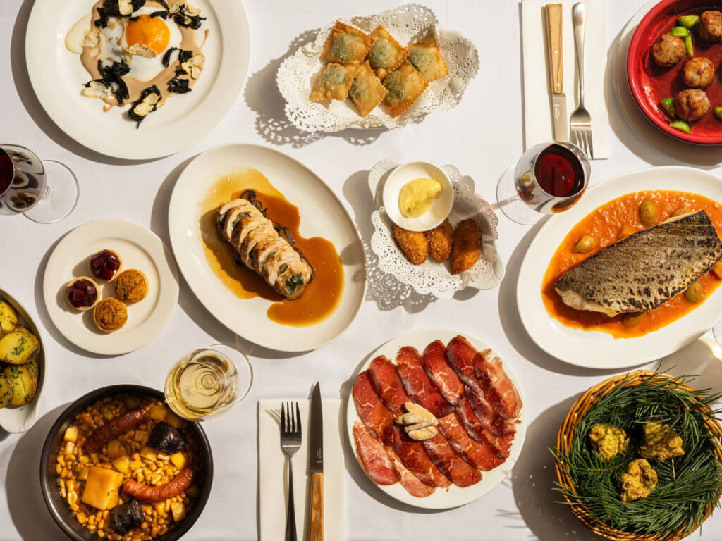 a table overladen with food dishes, ranging from fish to fried ravioli, cured meat, and more