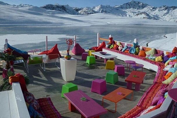 image of a terrace in the sun in the mountains, with bright coloured bench and tables and chairs. 