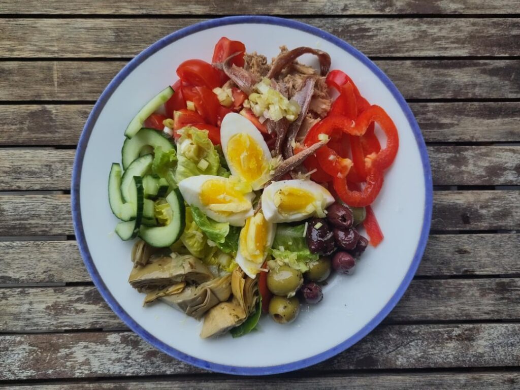 Salade niçoise — tomatoes, eggs, tuna, anchovies, artichokes, olives, lettuce, bell pepper, and cucumber