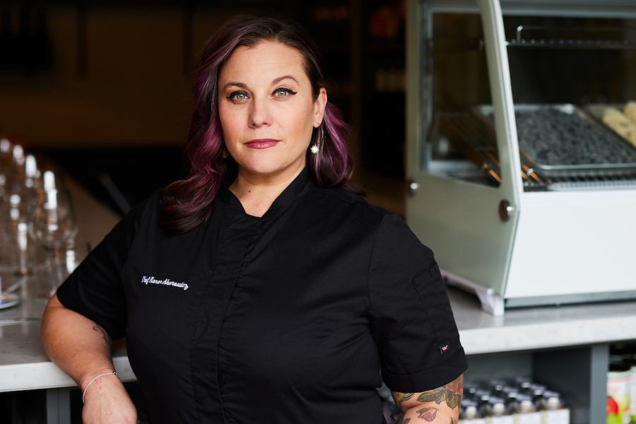 A woman in a black chef's shirt and pink streaks in her hair poses for a headshot.
