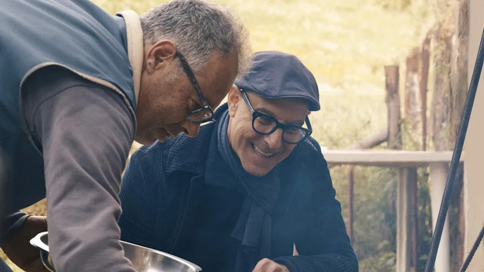  Stanley Tucci smiling as he kneels over a grill in Tucci in Italy. 