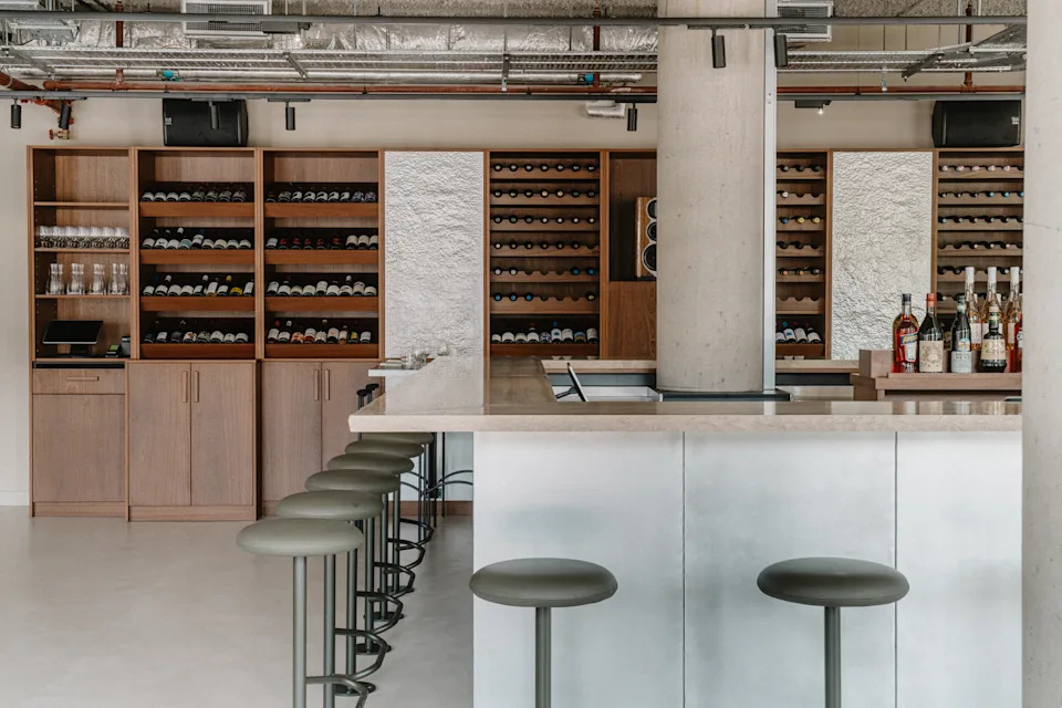 A sun-lit restaurant features brutalist interiors paired with a minimalist, black wrought iron-furnished canal-view terrace.