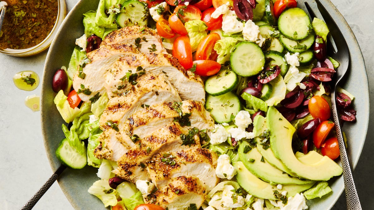 salad topped with sliced grilled chicken, cucumbers, cherry tomatoes, olives, and feta