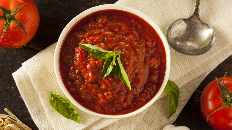 a top-down view of a white bowl of marinara sauce with basil on top of it.