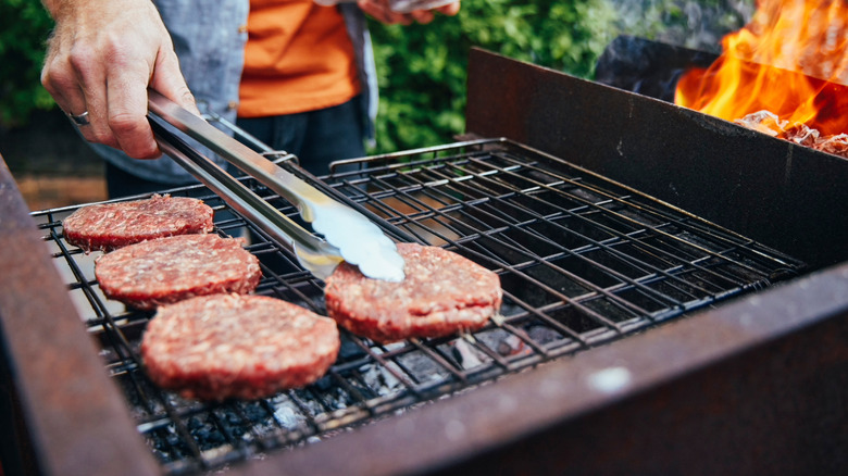 Man putting raw hamburgers on grill with tongs