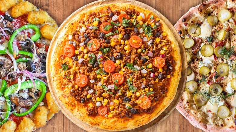 A pizza with tator tots and veggies, one with corn and beans, and a pickle and dill pizza on a wood background