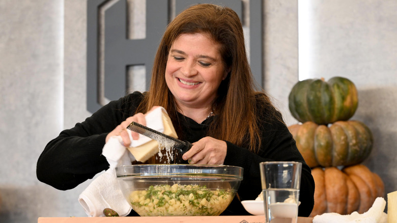 Alex Guarnaschelli smiling as she grates cheese into a bowl of pasta