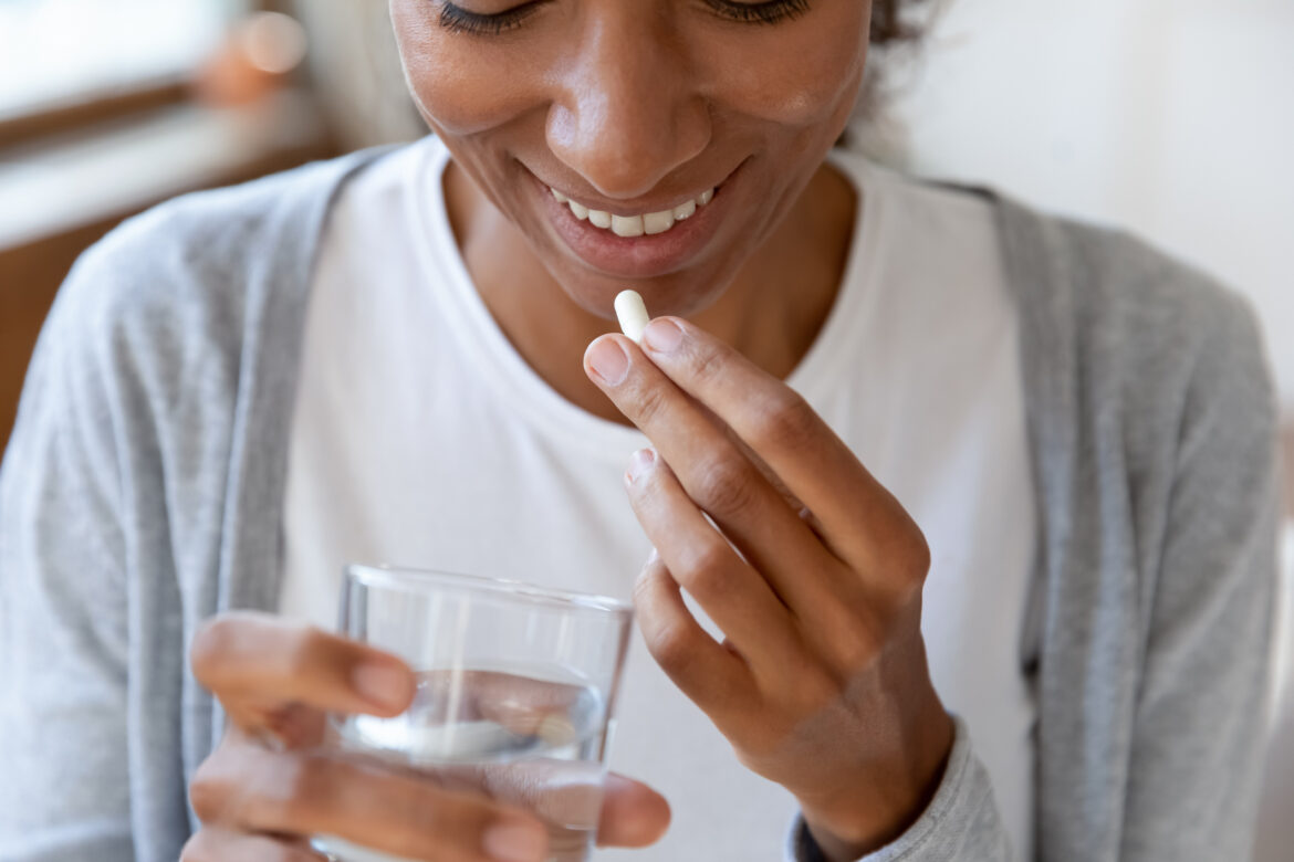 Woman holding a glass of water brings a pill towards her lips