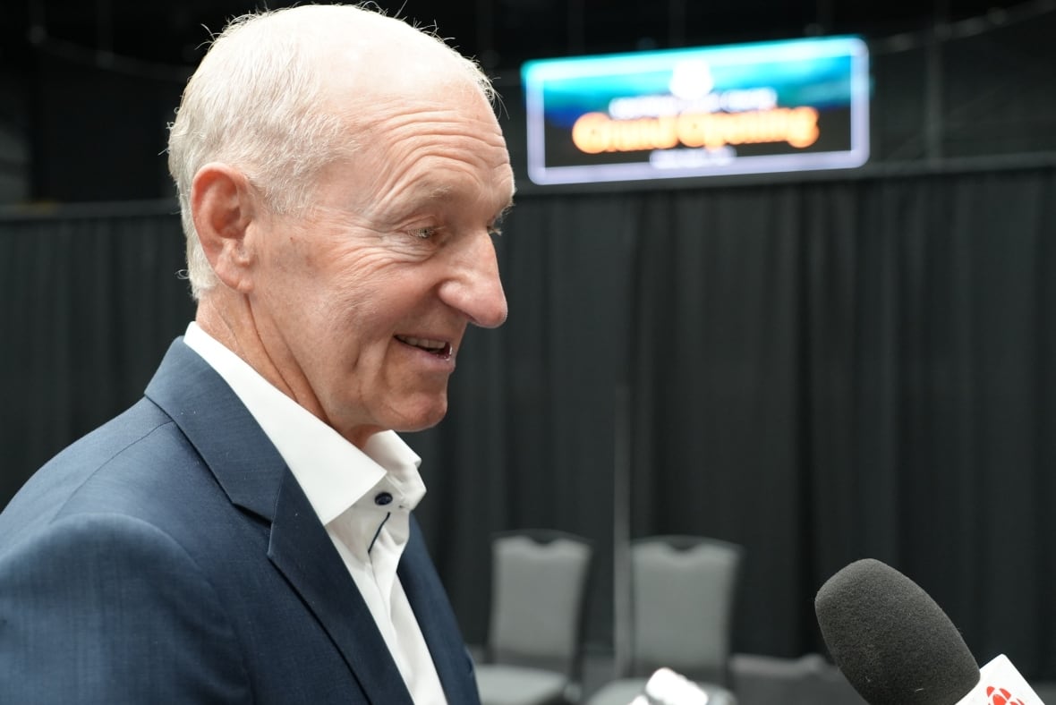 Man with white hair and blue suit speaks into a microphone.