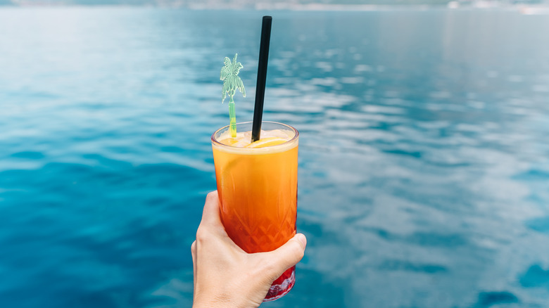 Person holding sex on the beach cocktail in front of water background