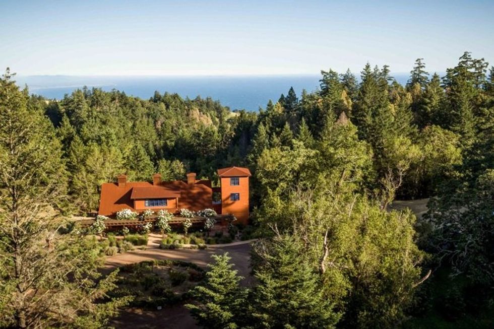 Rustic house amidst dense forest with distant sea view.