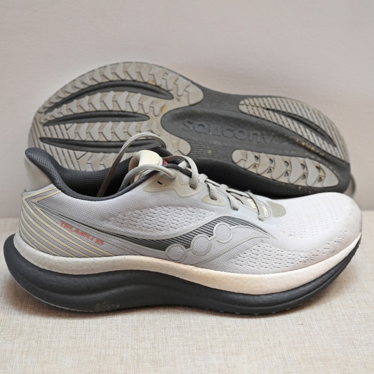 A close up shot of the Saucony Triumph 23 in a gray colorway, placed on top of a fabric bench.