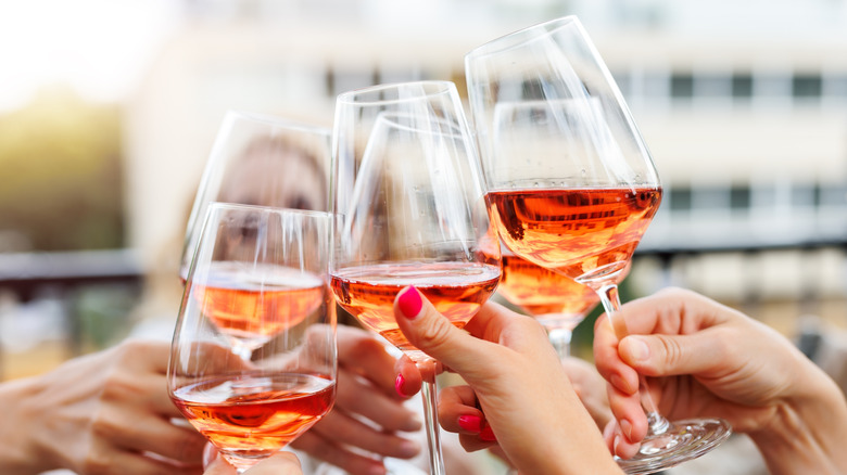 Hands holding pink/orange wine and clinking glasses