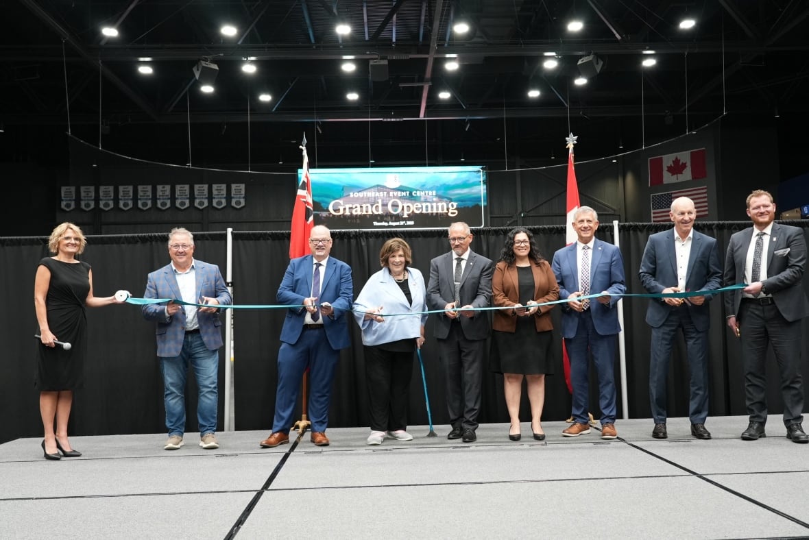 A line of people cutting a long blue ribbon on a stage.