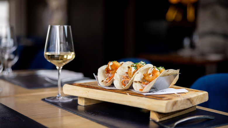 Glass of wine next to three plated tacos at restaurant