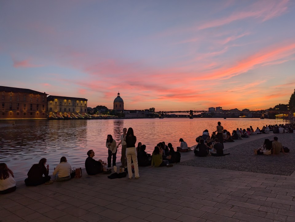 People gathered by a river at sunset in Toulouse.