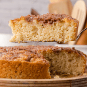 one slice of apple cake on a spatula above the rest of the apple cake on a wooden cake stand