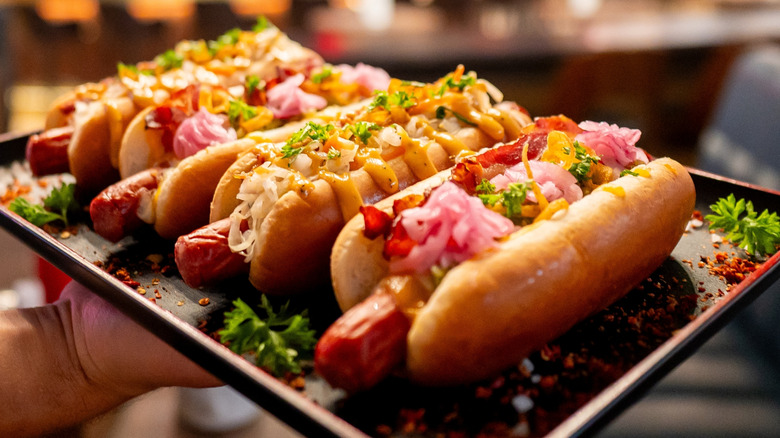 Hot dogs with different toppings on a black tray held by a hand