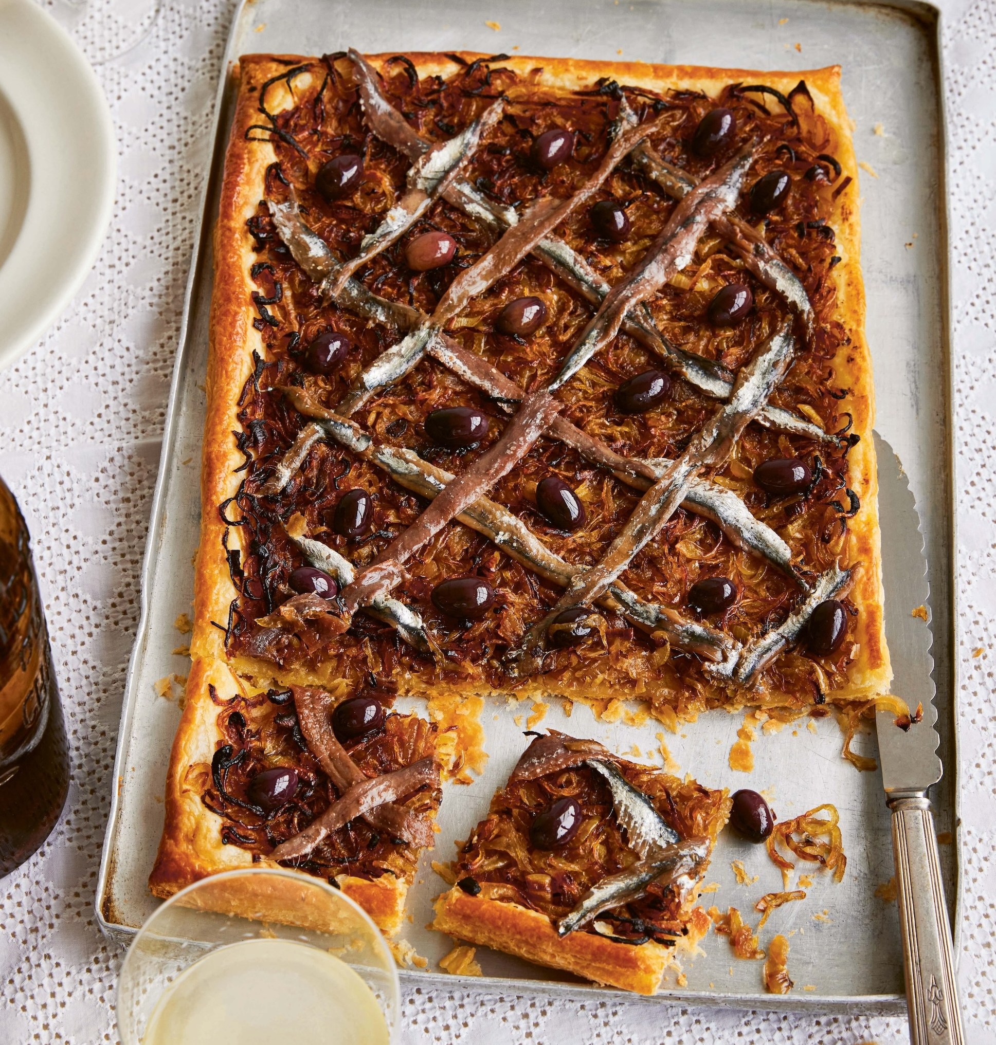 Pissaladière on a baking sheet with olives and anchovies.