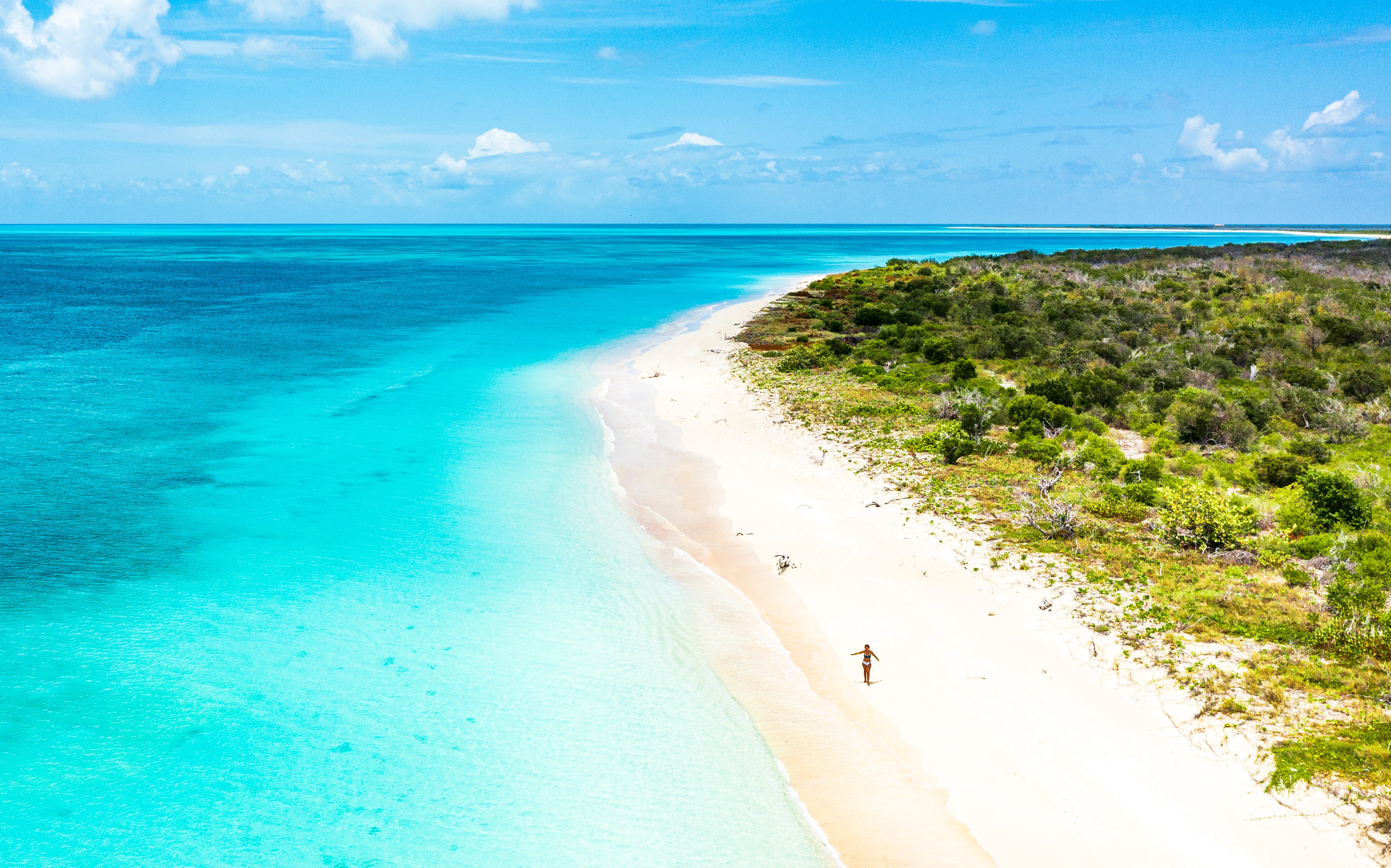 Aerial view of a woman in a bikini walking on a white sand beach.