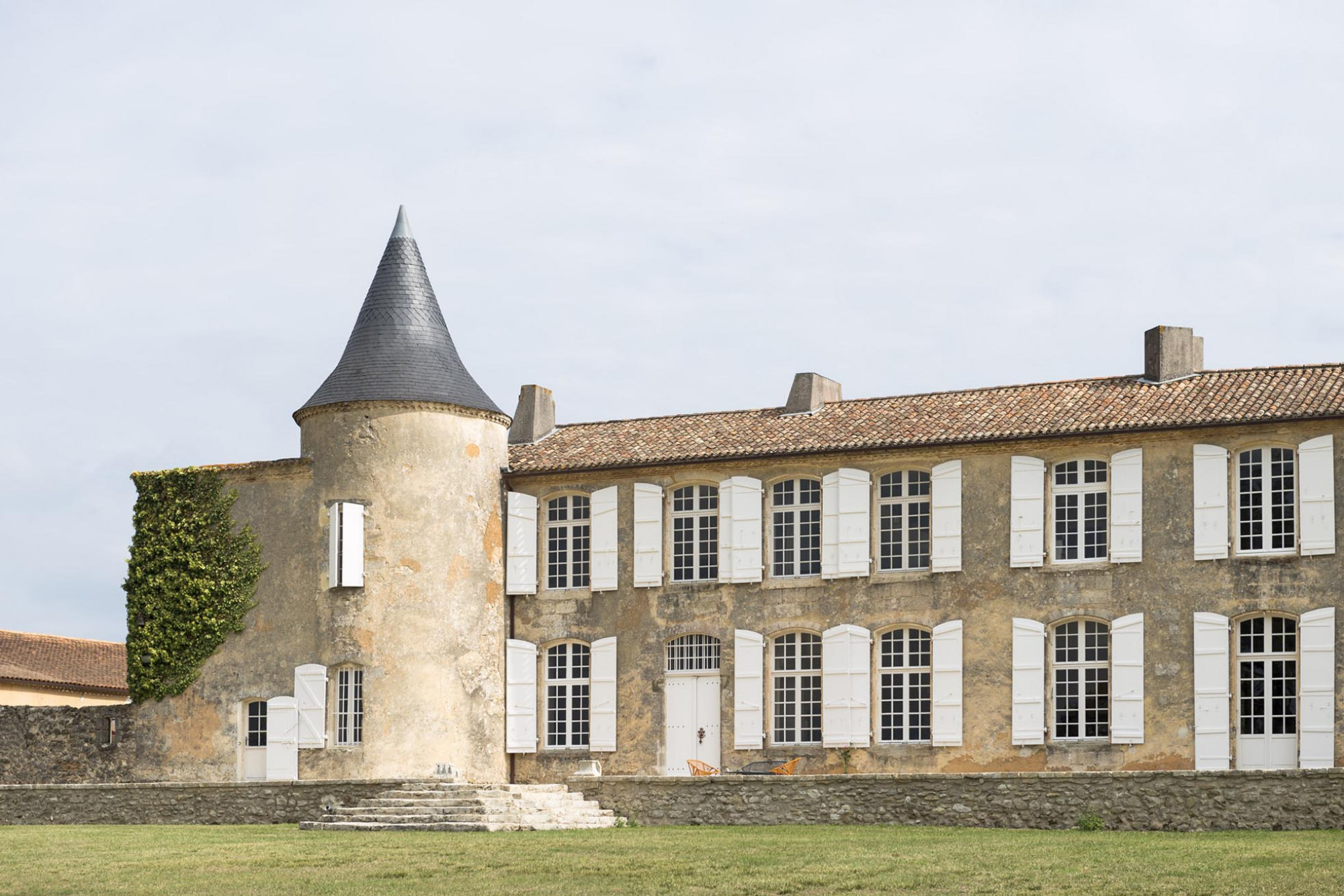 Stone manor house with a conical tower and white shutters.