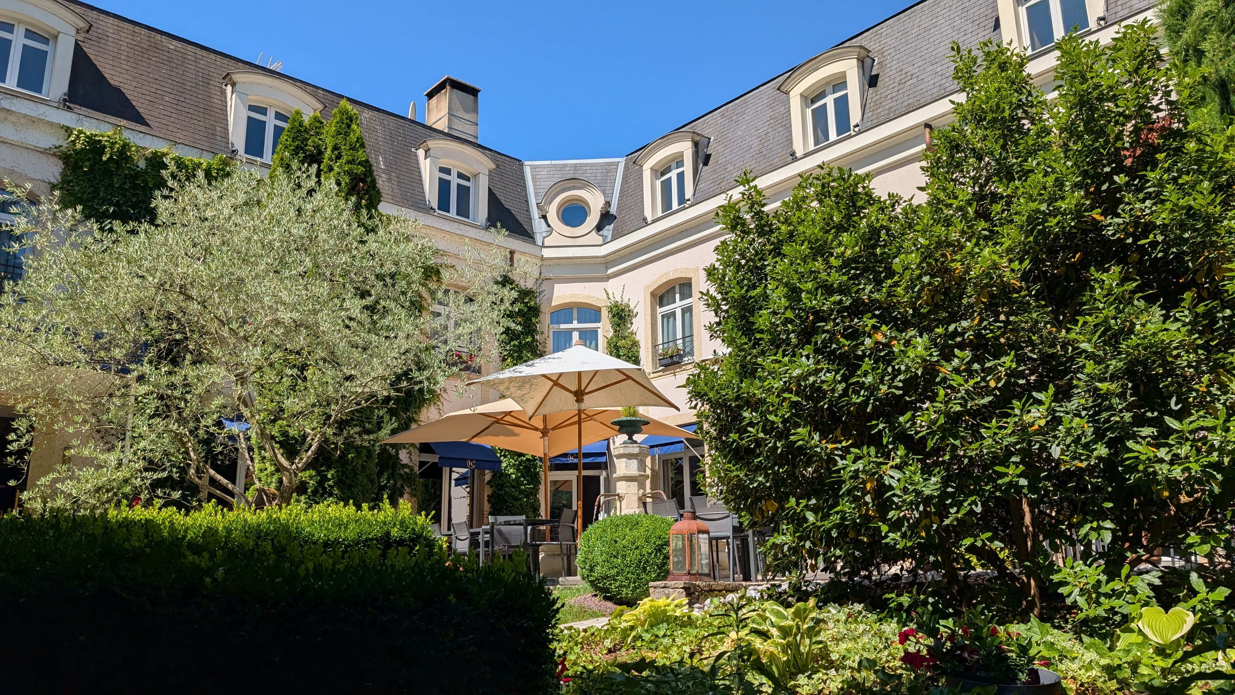 Courtyard patio with umbrellas and lush greenery next to a building.
