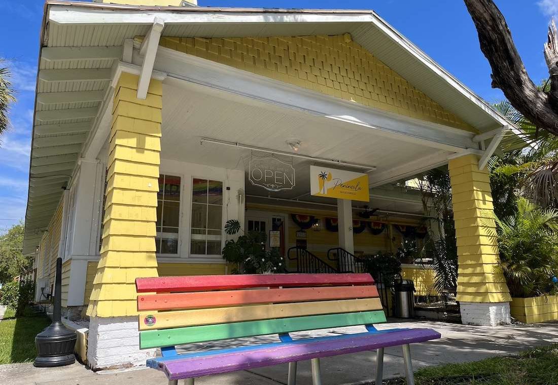 a rainbow bench outside a yellow building.