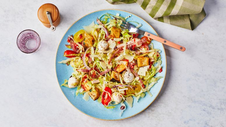 Italian grinder salad with shredded iceberg mini mozzarella balls peppadew peppers Fontina cheese and croutons on a blue...