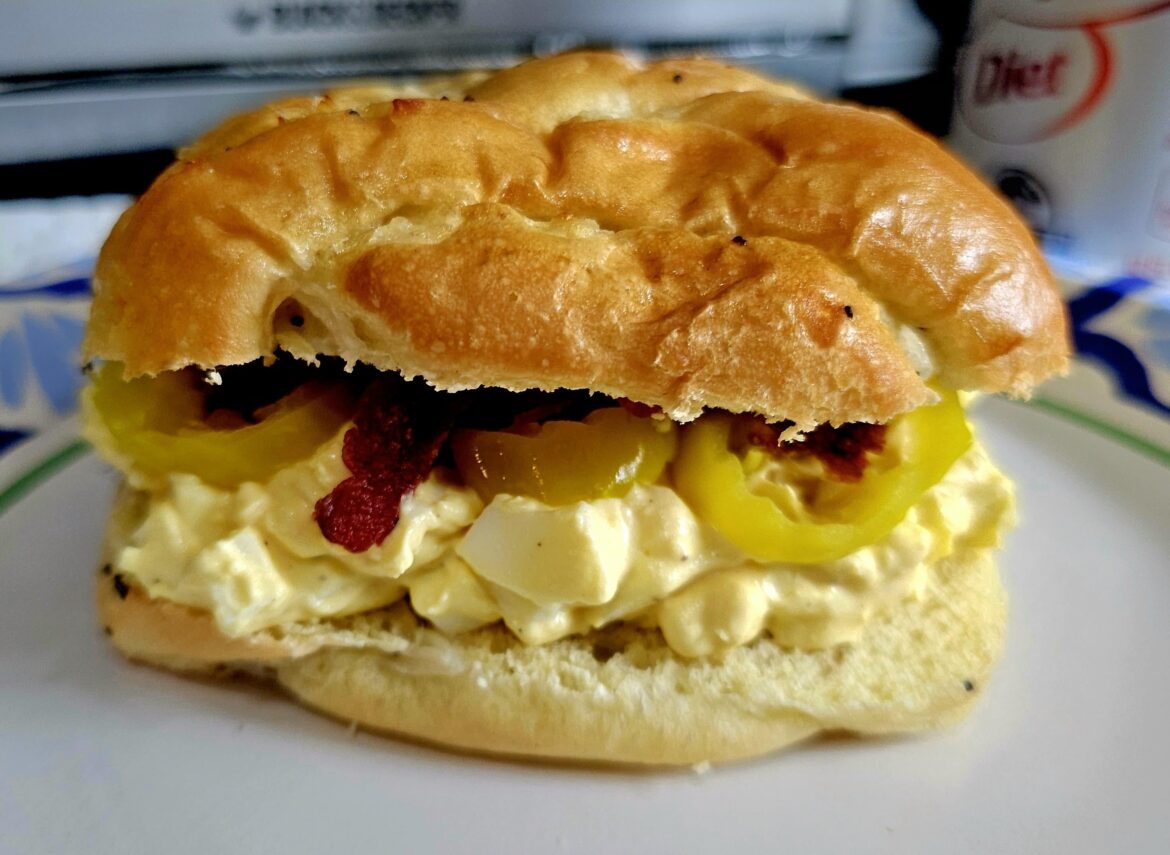 Fresh egg salad with banana peppers and bacon on an onion roll.