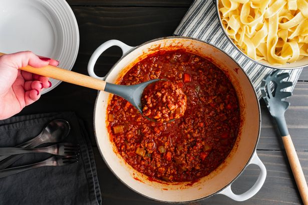 Ragu alla bolognese Italian tomato and meat sauce in a spoon held over a large pot