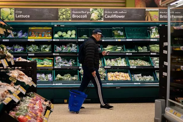A shopper walks through the salad aisle in a branch of Tesco looking at their phone 