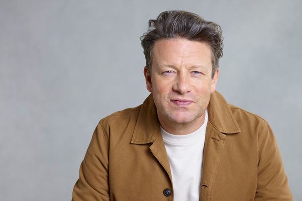 Jamie Oliver against grey backdrop with plate of food