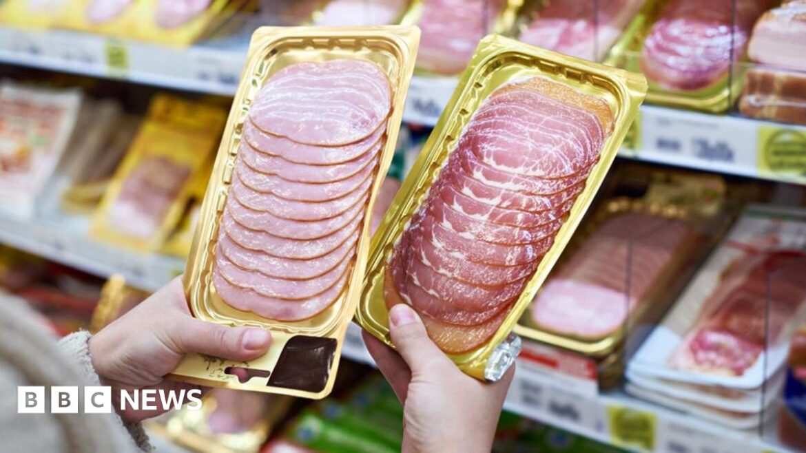A close up of a womans hands holding two packets of cured meats in a shop
