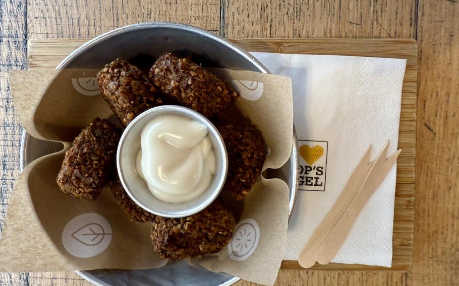 A plate of golden-brown  falafel arranged in a metal bowl with a small container of white dipping sauce in the center, served on brown paper with wooden utensils.