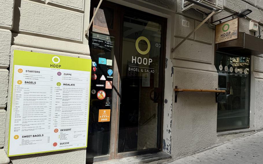 Street-front exterior of HOOP Bagel & Salad restaurant showing the storefront entrance, yellow menu board posted outside, and the restaurant’s green circular logo on the window and signage.