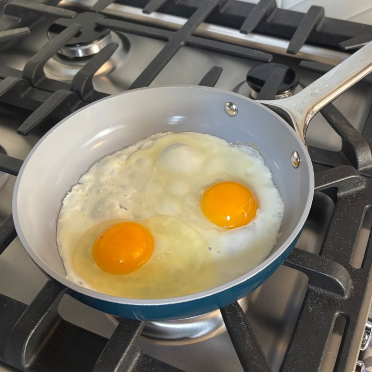 Two eggs in Caraway’s Nonstick Ceramic Frying Pan over a gas stove.