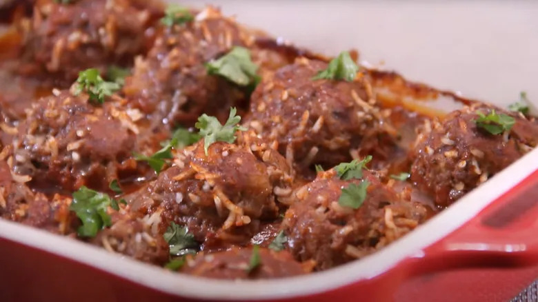 porcupine meatballs in a baking dish with tomato sauce and herb garnish