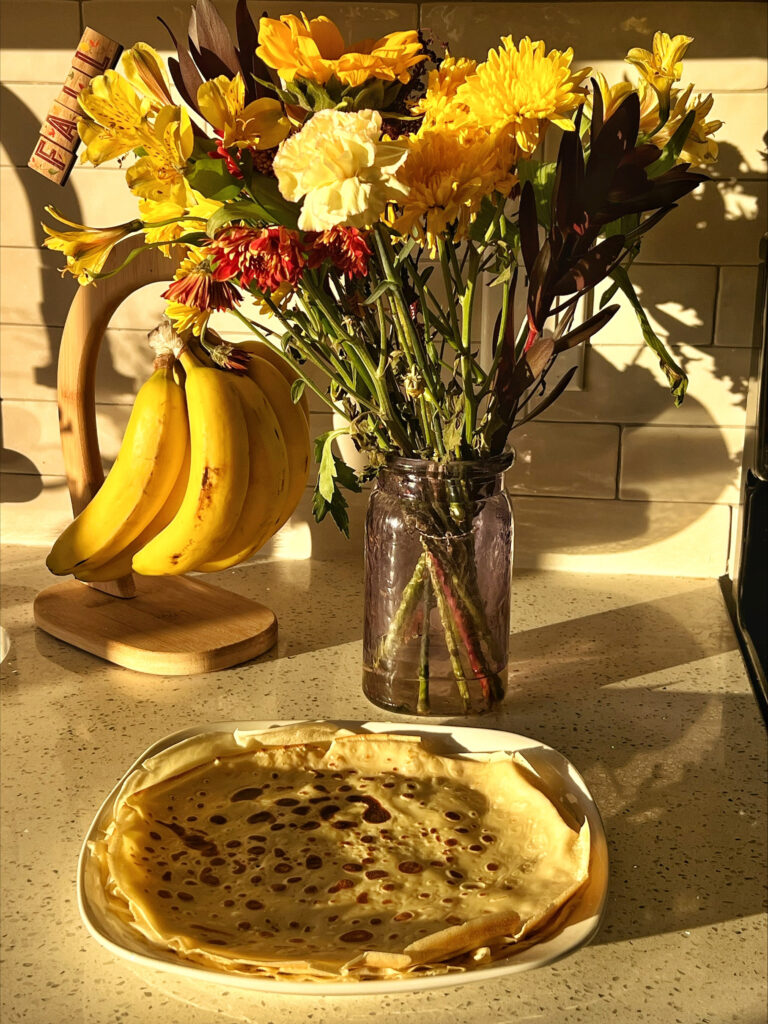 Crepes on a plate next to a vase of flowers