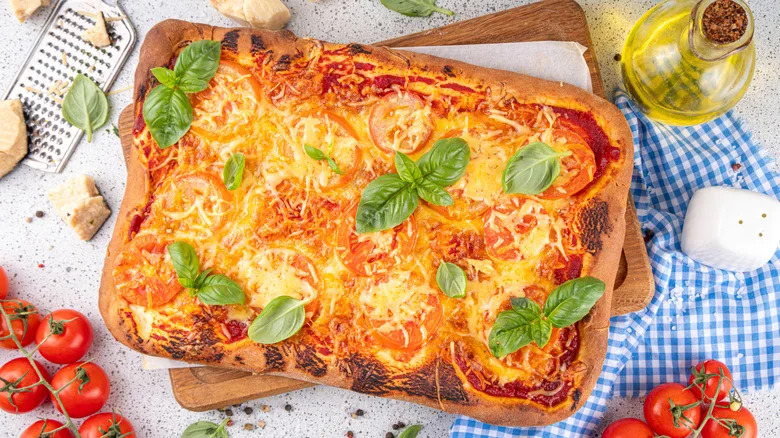 Rectangular pizza with tomoatos, olive oil, and checked napkin