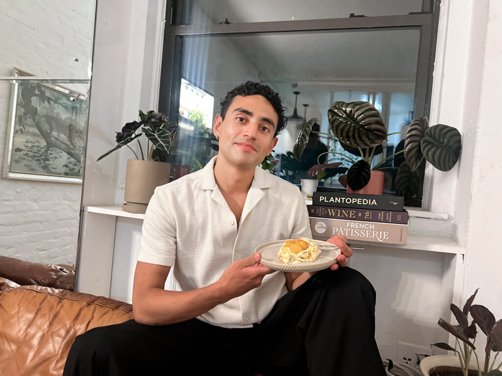 Miguel Solano sitting on his couch holding a plate of banana pudding. 