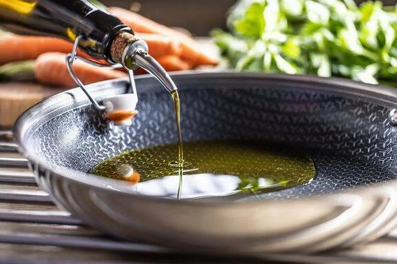 Olive oil is poured from a bottle into a modern non-stick frying pan